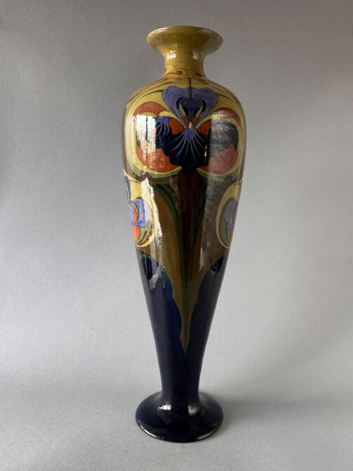 Vaas, model 112 van Firma Jb Vet uit Purmerend. 43 cm hoog en 13 cm breed met een bont floraal decor met irissen, gemaakt tussen 1903 en 1907.