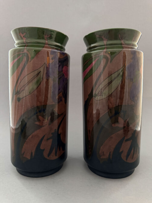 paar vazen van Plateelbakkerij Zuid-Holland uit Gouda, uit de periode 1899-1902. Dit is model 108 een cilinrisch ontwerp met een typisch vroeg Gouda-decor met paarse bloemen tegen een bruine achtergrond. De vazen zijn beschilder door Adriaan Lansaat en Michel van der Heidt.