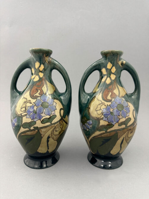 Twee vazen van Plateelbakkerij Zuid-Holland uit de periode 1900-1905,model 138 met oren en beschilderd met paarse bloemen door Hendrikus Houdijck.